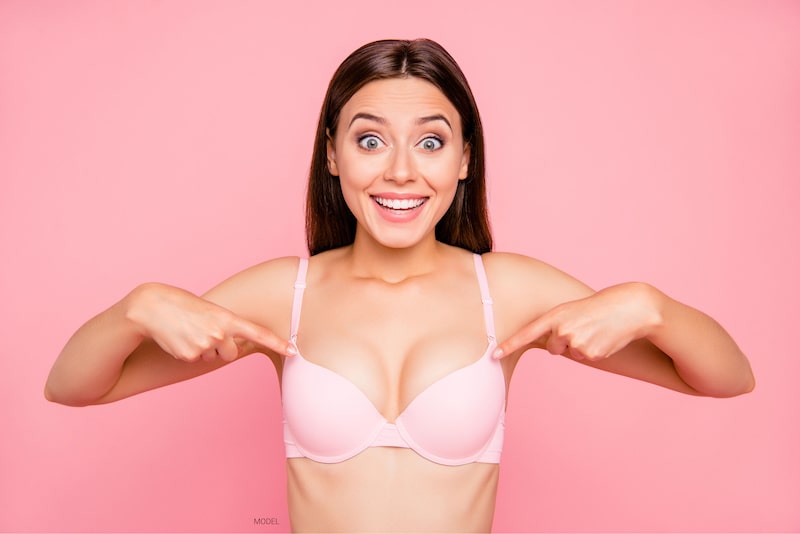 A happy woman points at the pink bra she's wearing.