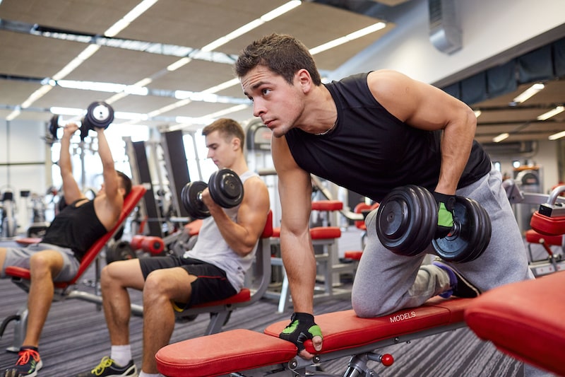 Man lifting weight at the gym with other men.