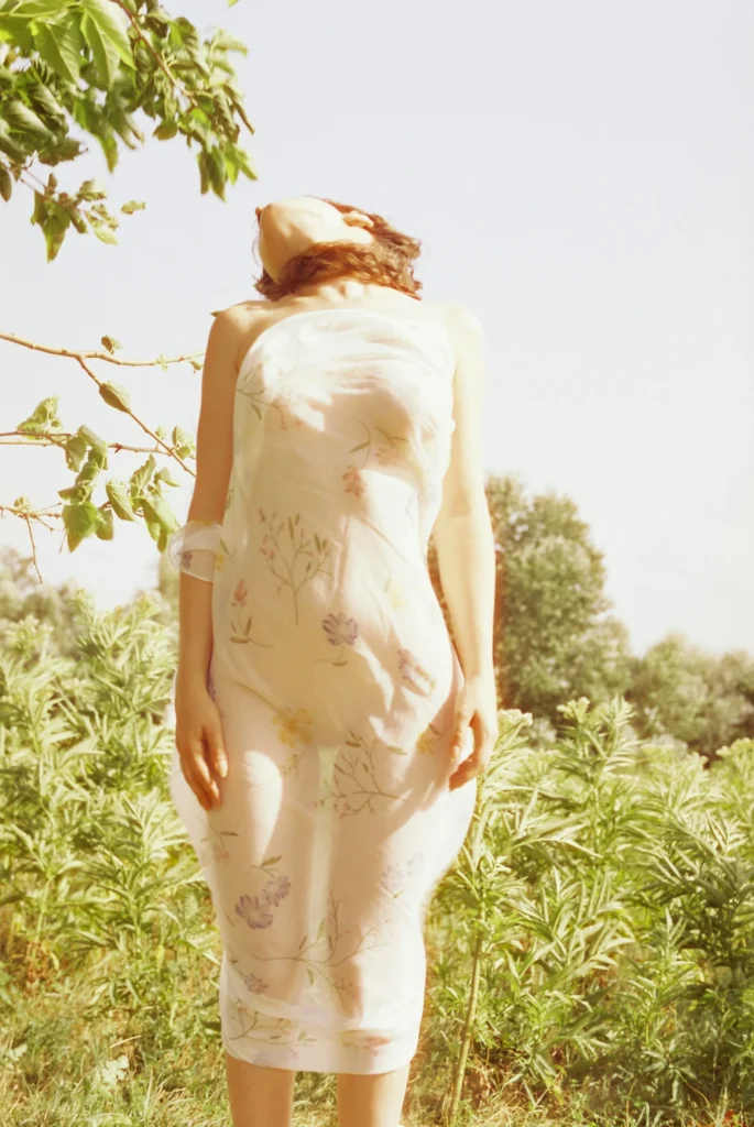 Image of a woman in a sheer floral dress standing in a sunlit garden, feeling free and at ease