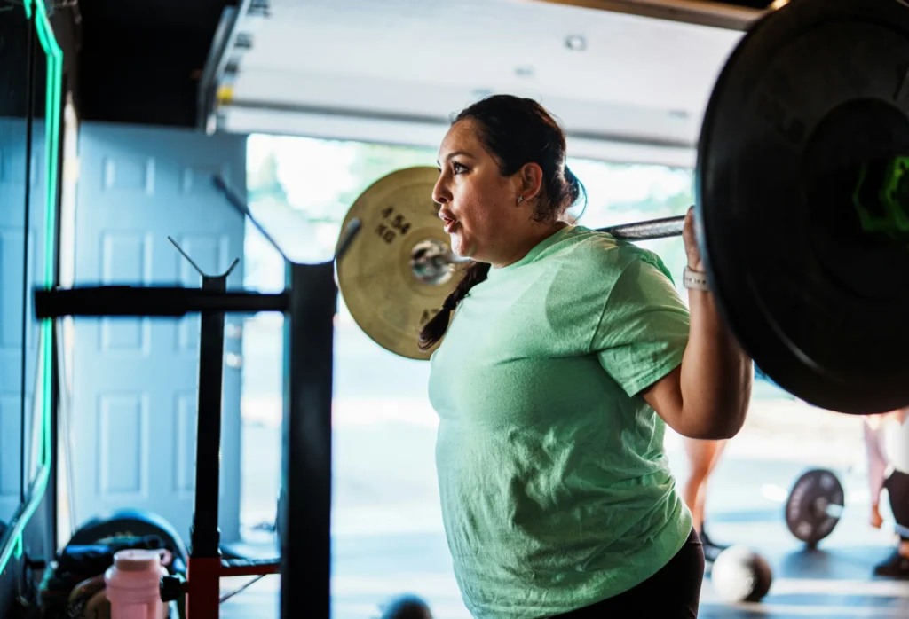 Image of a woman with large breasts lifting a barbell at the gym, showing exercise difficulty caused by big breasts